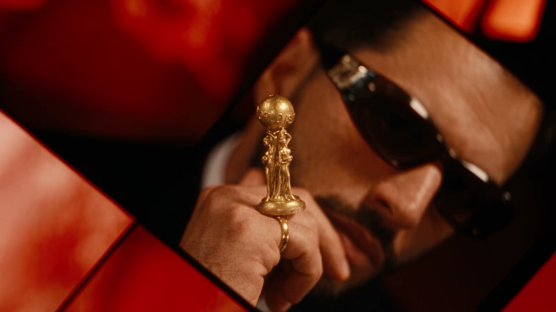 Source frame of a hand holding a small gold trophy in front of a red car interior, sunglasses in reflection